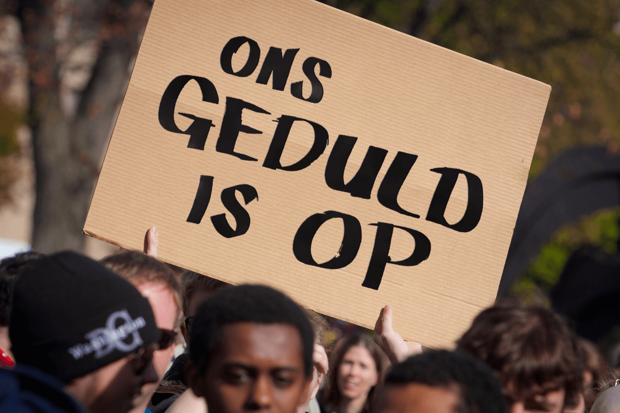 Mensen demonstreren en houden een bord op met de tekst 'Ons geduld is op'.
