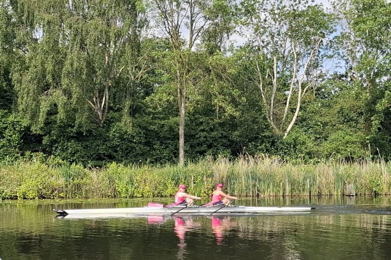 Inge en Denise al roeiend op het water met riet en bomen op de achtergrond